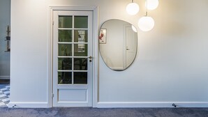 Uma porta branca com um painel de vidro, um espelho redondo na parede e três luminárias esféricas penduradas.