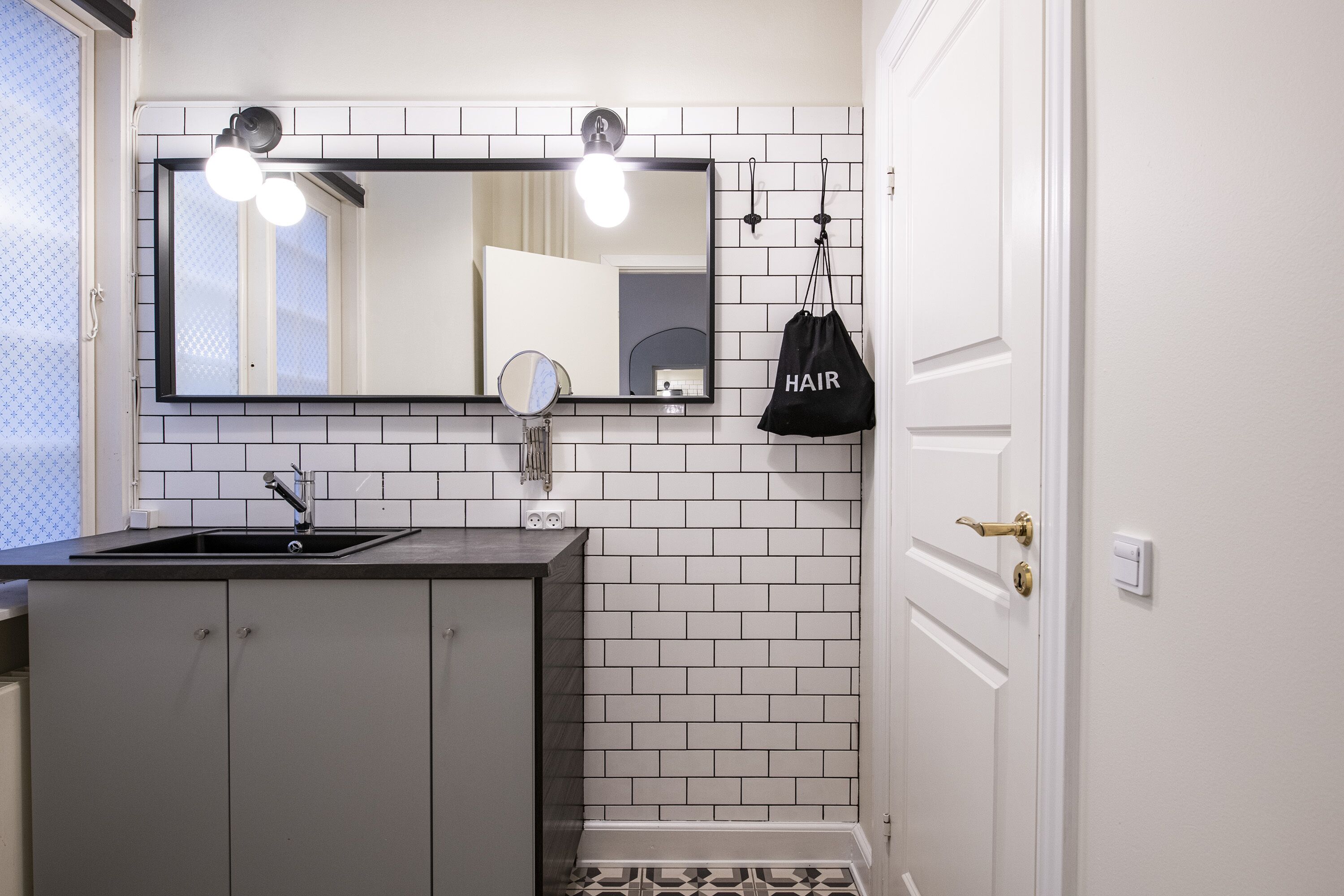 Un bagno con parete in piastrelle bianche, uno specchio grande, un lavandino e una porta.