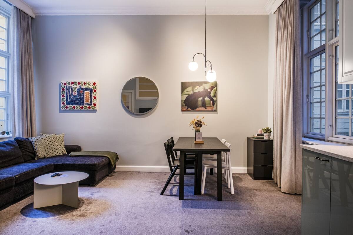 Una sala de estar moderna con un sofá, una mesa de centro redonda, una mesa de comedor con sillas, un espejo y obras de arte en las paredes.