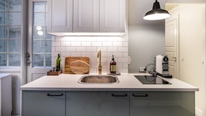 Cozinha com bancada branca, pia de aço inoxidável e luminária pendente moderna.