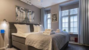 Een keurig opgemaakt bed met een gewatteerde spreideken, een bedlampje en een wanddecoratie van zwanen.