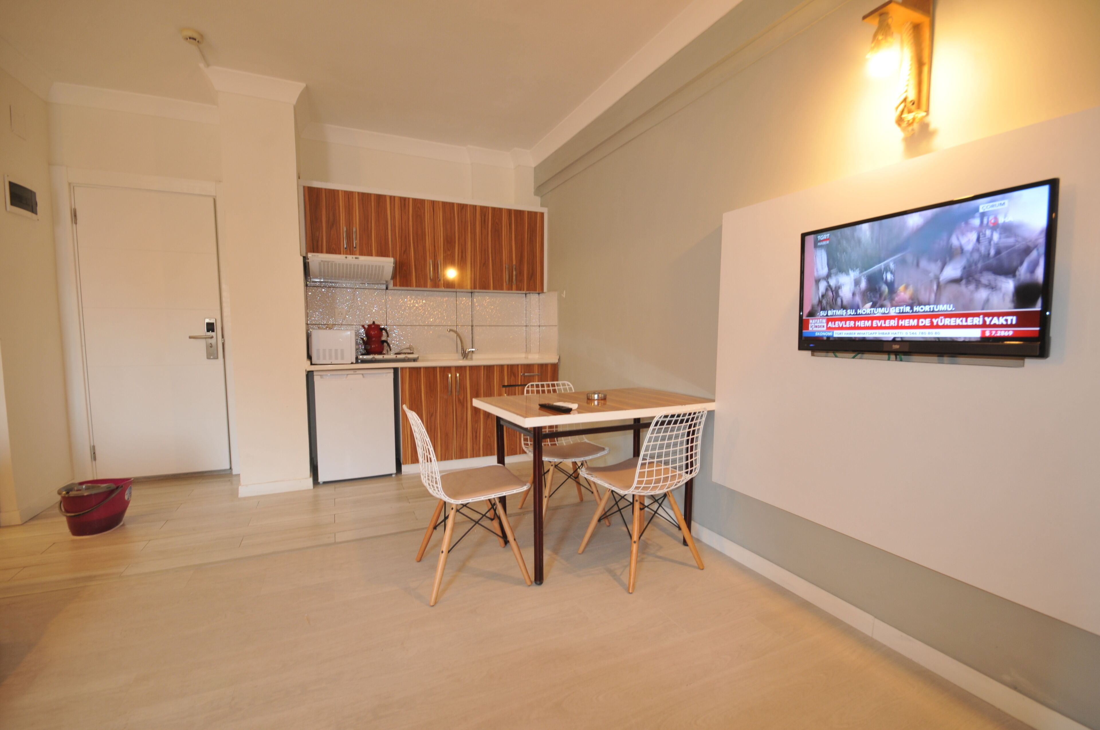 A modern kitchen with wooden cabinets, a dining table with chairs, and a television mounted on the wall.