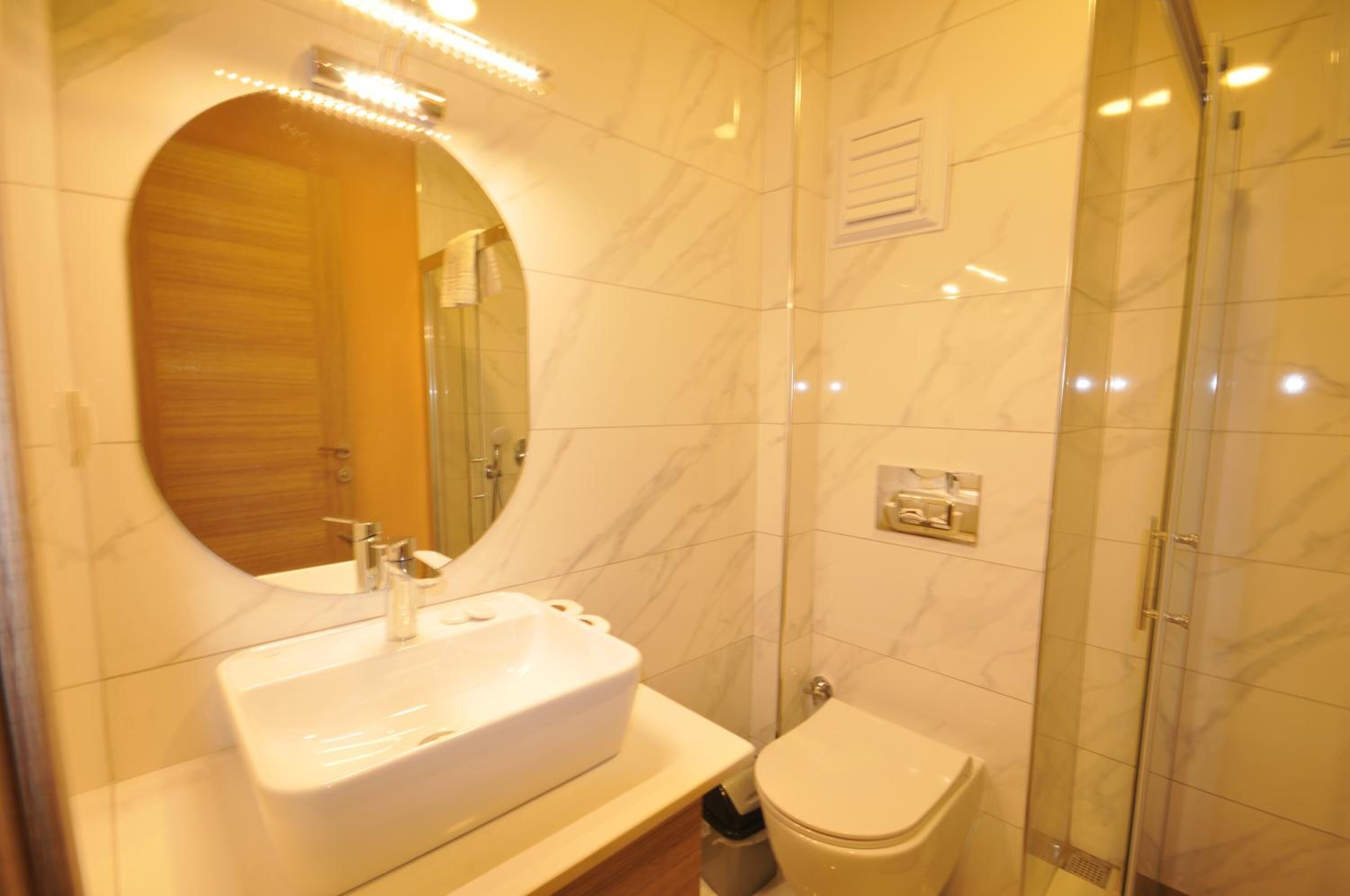 Un baño con lavamanos de mármol, inodoro y ducha con mampara de vidrio.