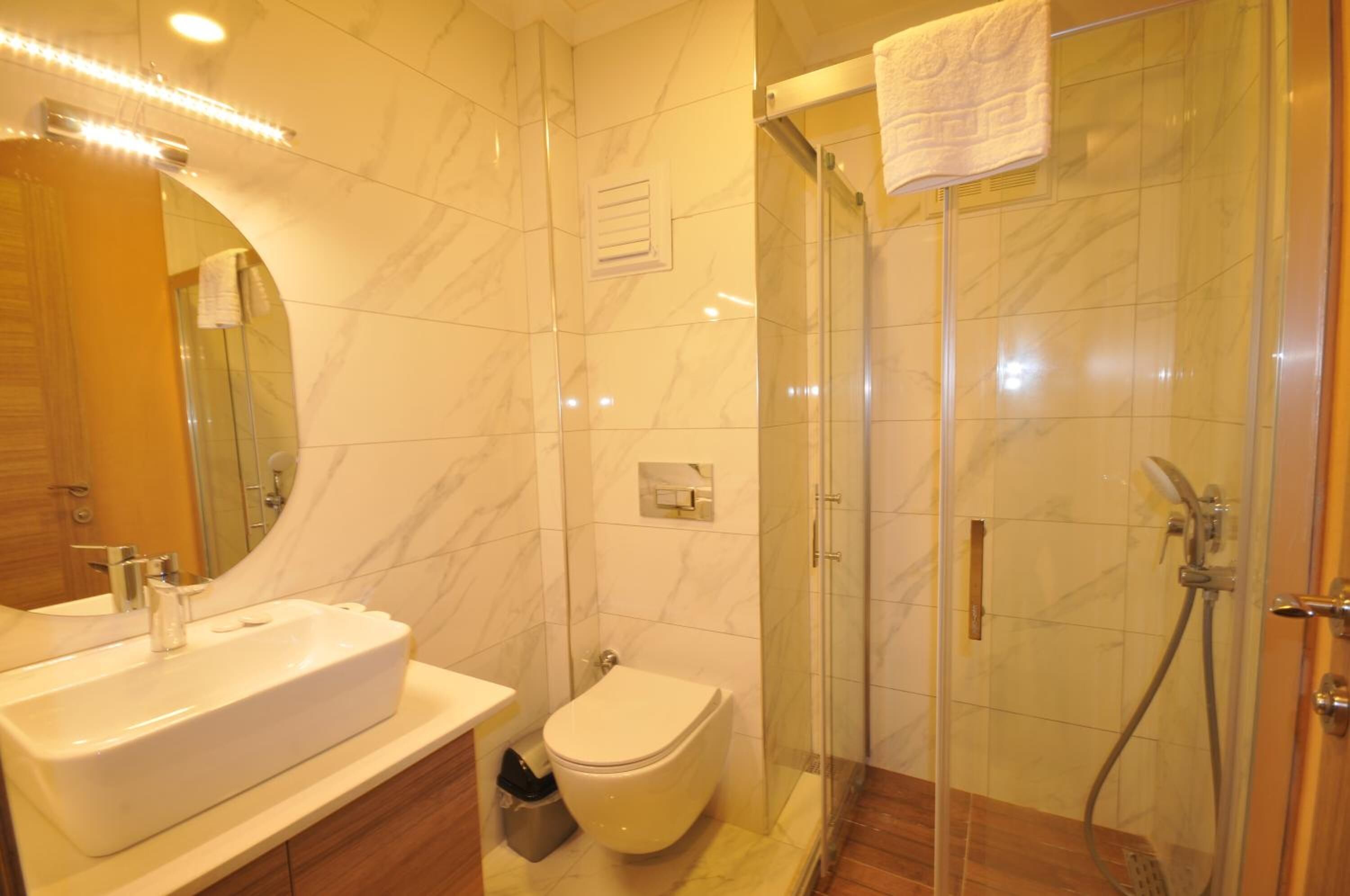 A modern bathroom with a marble sink, toilet, and glass-enclosed shower.
