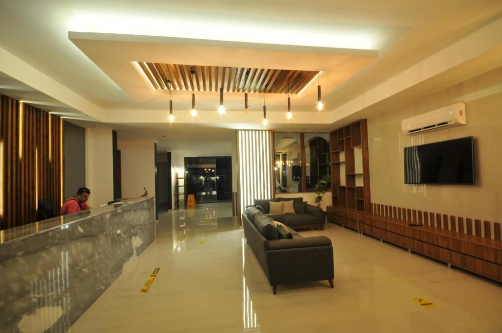 A hotel lobby with a reception desk, a sofa, a TV, and a wooden panel ceiling.