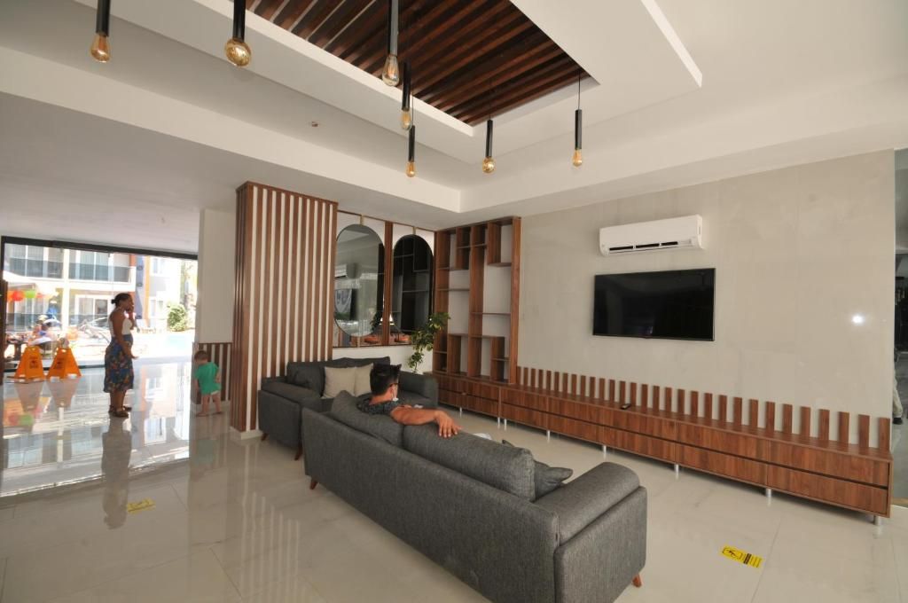A modern living room with a large grey sofa, a flat-screen TV mounted on the wall, and a wooden bench along the wall.