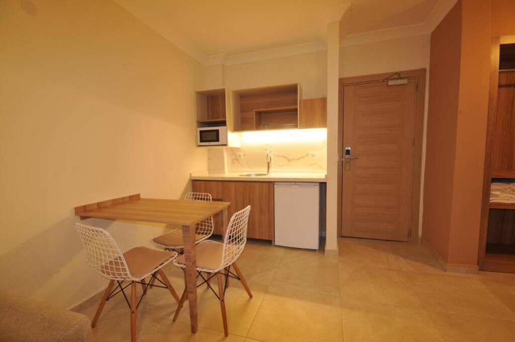 A compact kitchen with a wooden table and white wire chairs, a microwave, and a small refrigerator.
