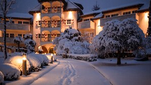 A snow-covered building with a symmetrical facade, a central entrance, and a pathway leading to the entrance. - Hotel Hanswirt (Parcines)