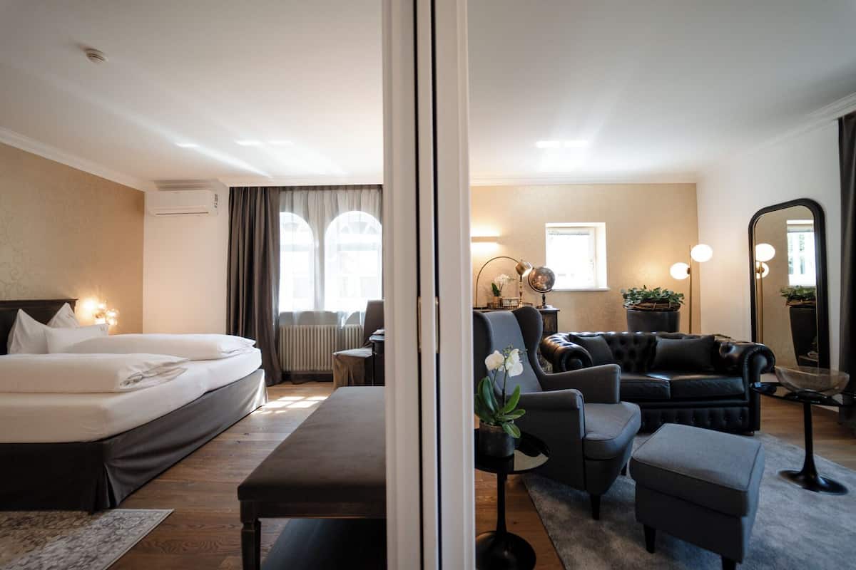 A hotel room with a bed, a sofa, a chair, a small table, and a mirror.
