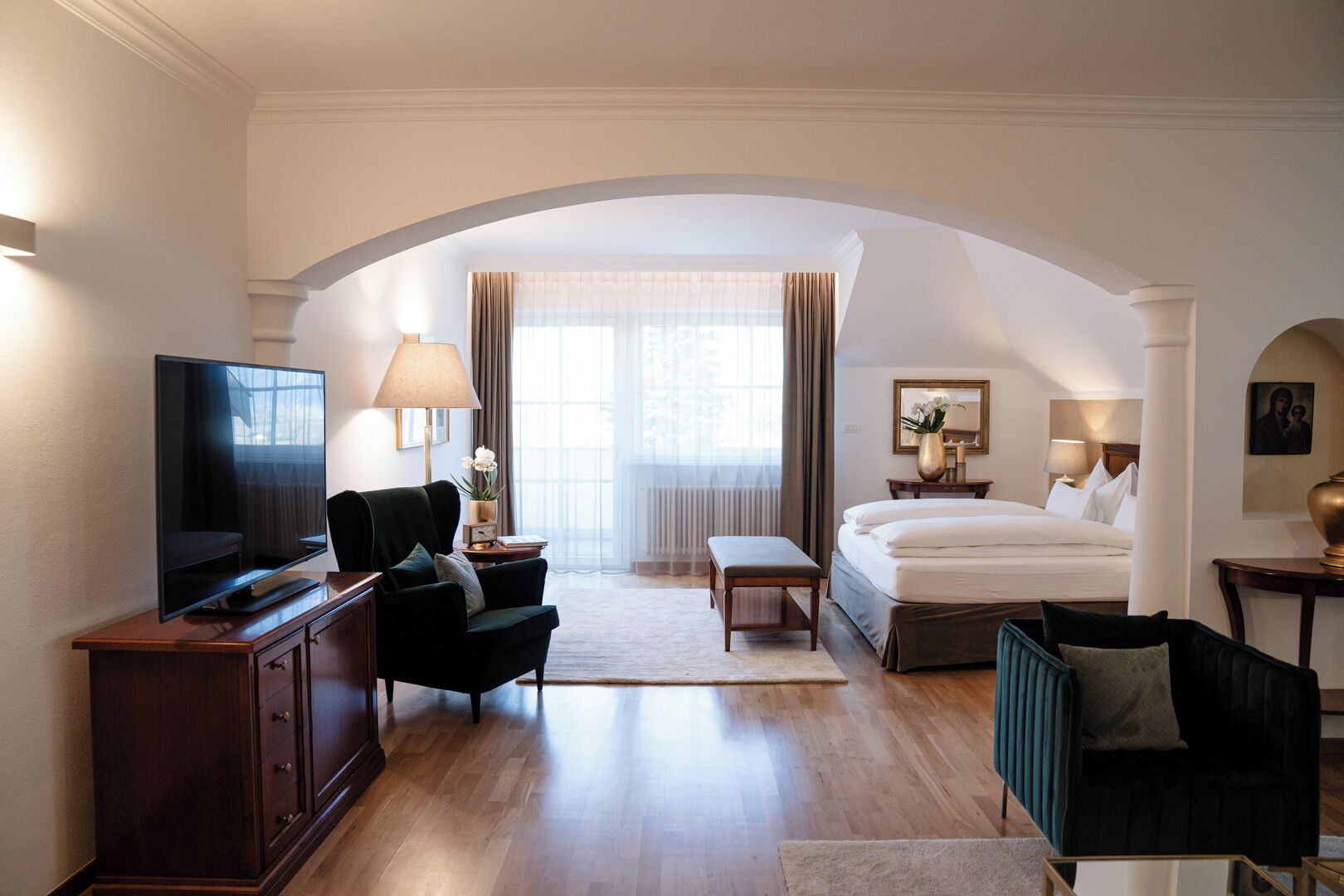 Habitación de hotel con televisión, sofá, cama, escritorio y ventana con cortinas.