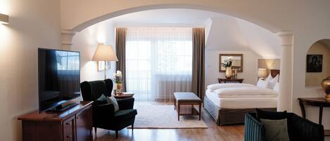 Habitación de hotel con televisión, sofá, cama, escritorio y ventana con cortinas.