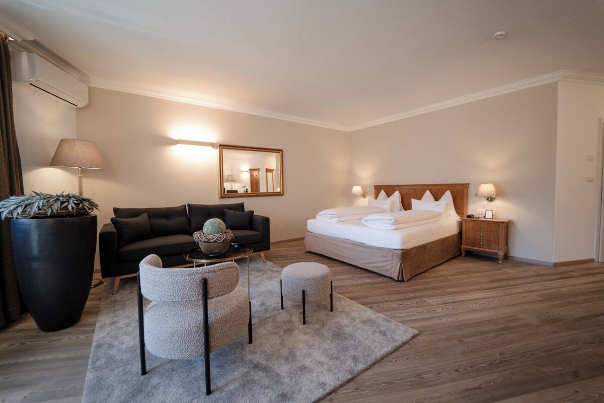 A modern hotel room with a large bed, a sofa, a coffee table, and a side table.