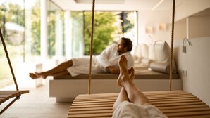 A person lying on a bed with a view of greenery outside. - Hotel Hanswirt (Parcines)
