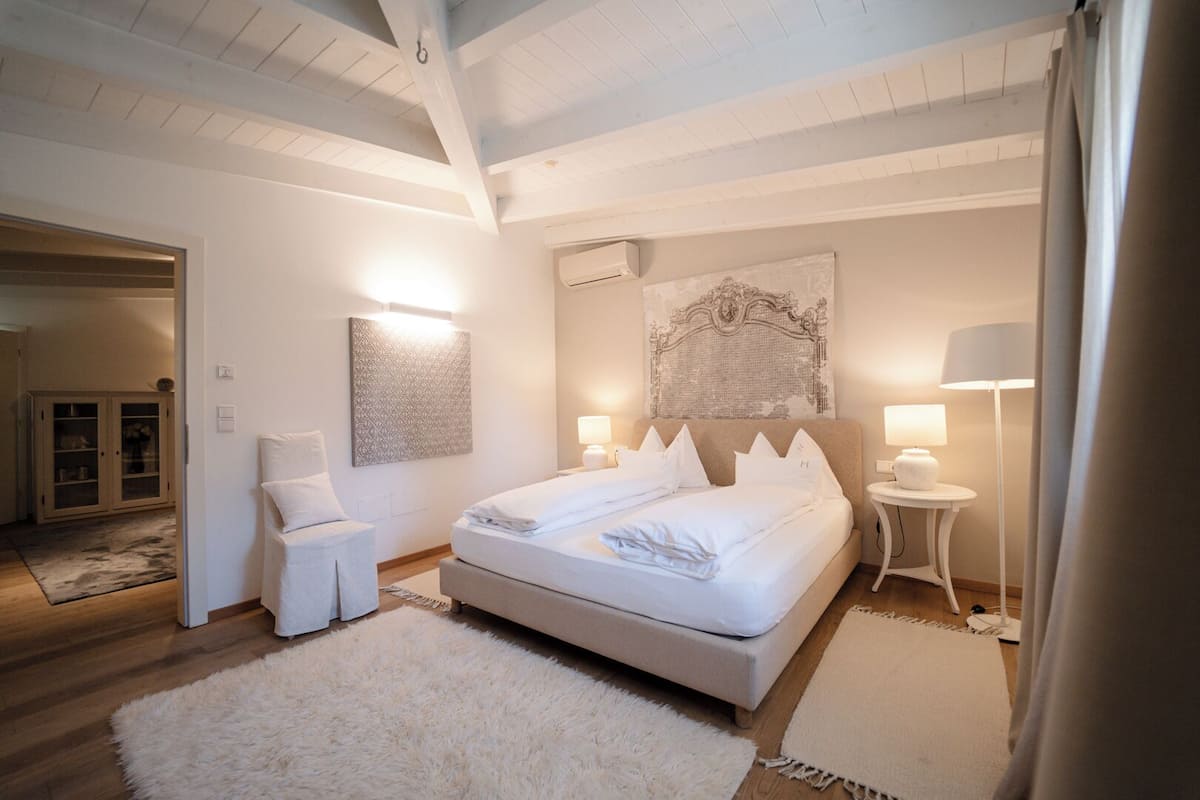 A bedroom with a large bed, a chair, a bedside table, and a lamp.
