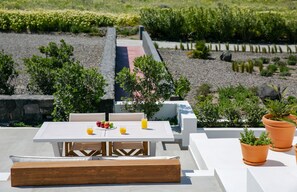 An outdoor patio with a table and chairs, surrounded by potted plants and a garden view.