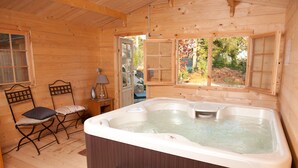 A wooden cabin interior with a hot tub, two chairs, a window, and a door leading outside. - Manoir Desnachez (Taupont)