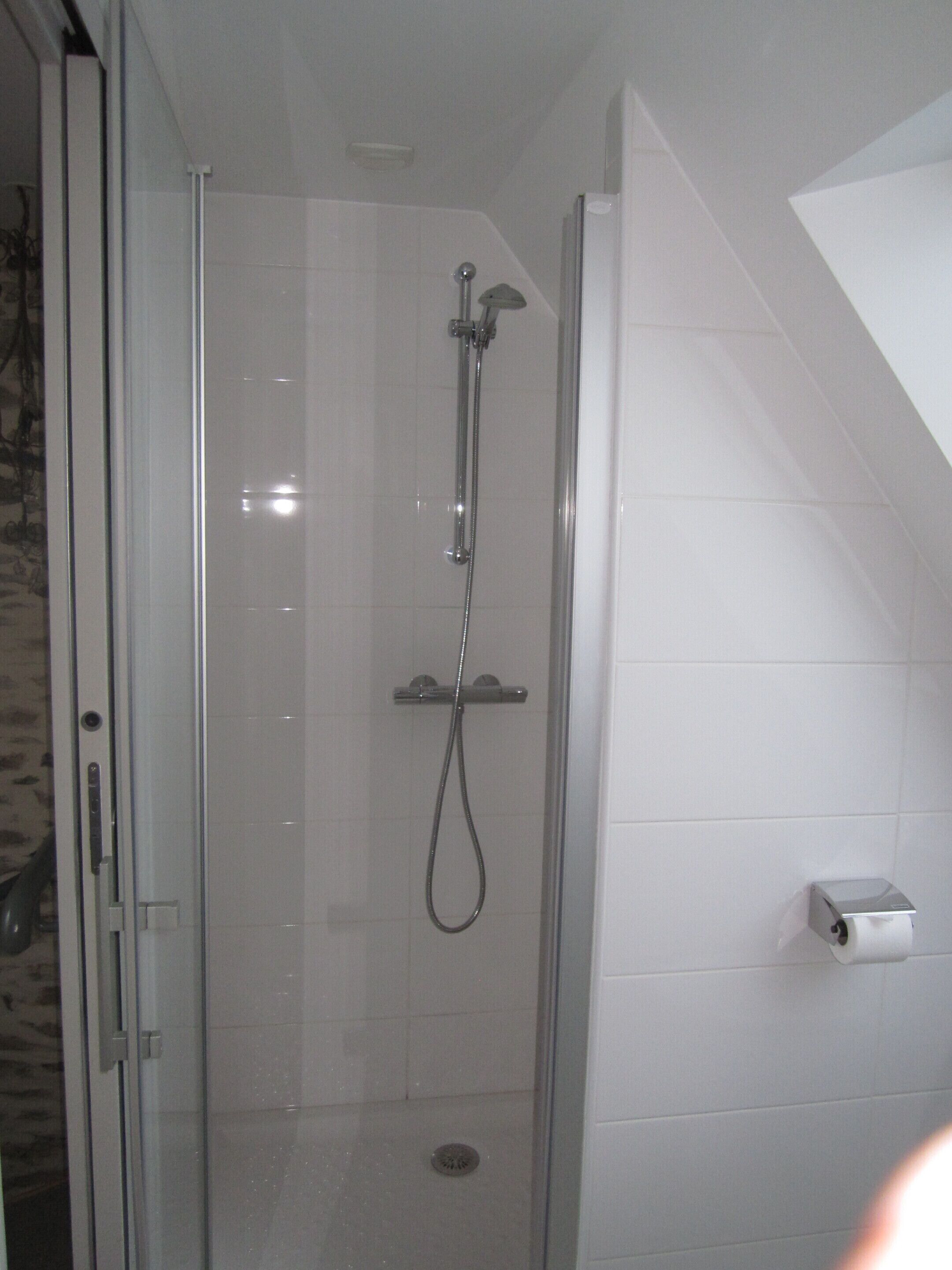 A glass-enclosed shower with a handheld showerhead and a wall-mounted faucet.