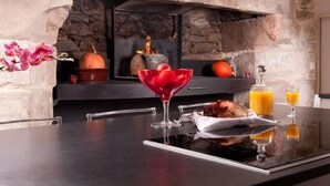 A modern kitchen with a stone fireplace, a glass table, and a decorative orchid. - Manoir Desnachez (Taupont)