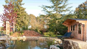 A wooden cabin with a pond, surrounded by trees and rocks. - Manoir Desnachez (Taupont)