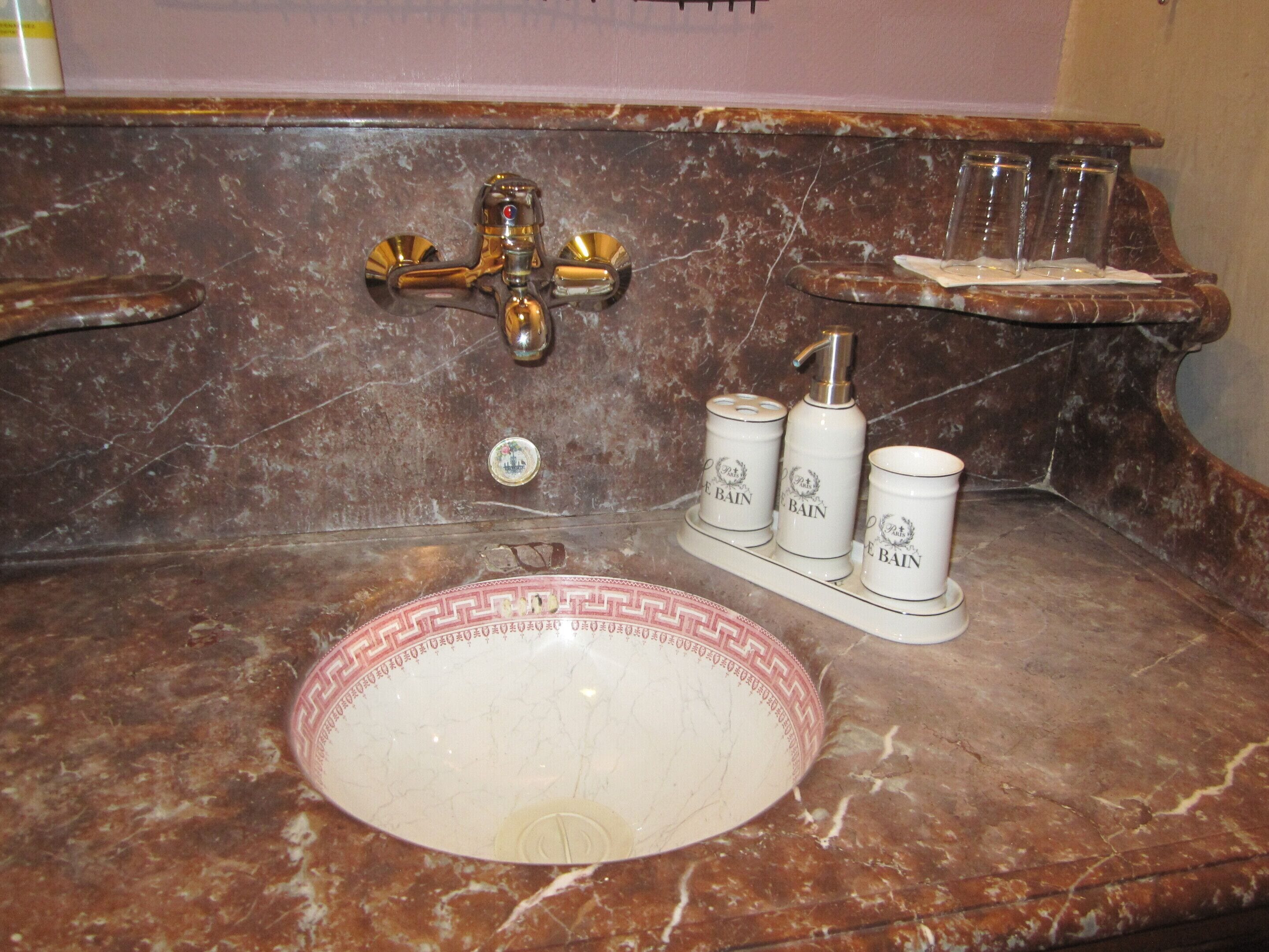 A bathroom with a marble sink, a gold faucet, and three toiletry bottles labeled "Le Bain".