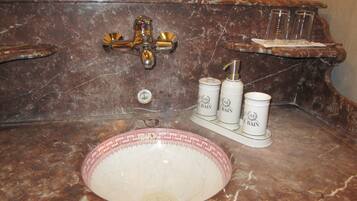 A bathroom with a marble sink, a gold faucet, and three toiletry bottles labeled "Le Bain".