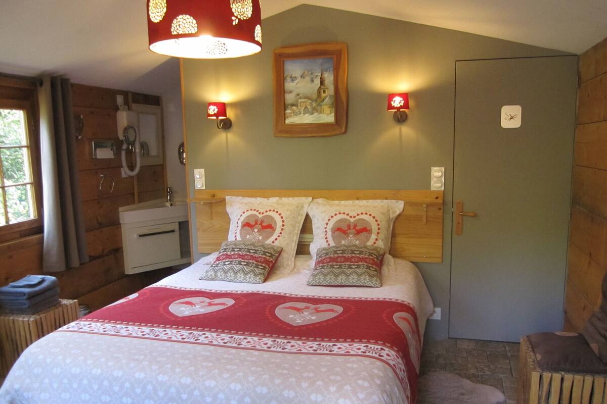 Une chambre confortable avec une tête de lit en bois, un lit avec une literie à motifs de cœurs, deux lampes de lecture fixées au mur et un tableau au-dessus du lit.
