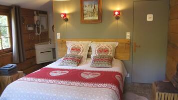 Een gezellige slaapkamer met een houten hoofdbord, een bed met beddengoed met een hartjespatroon, twee wandlampen en een schilderij boven het bed.