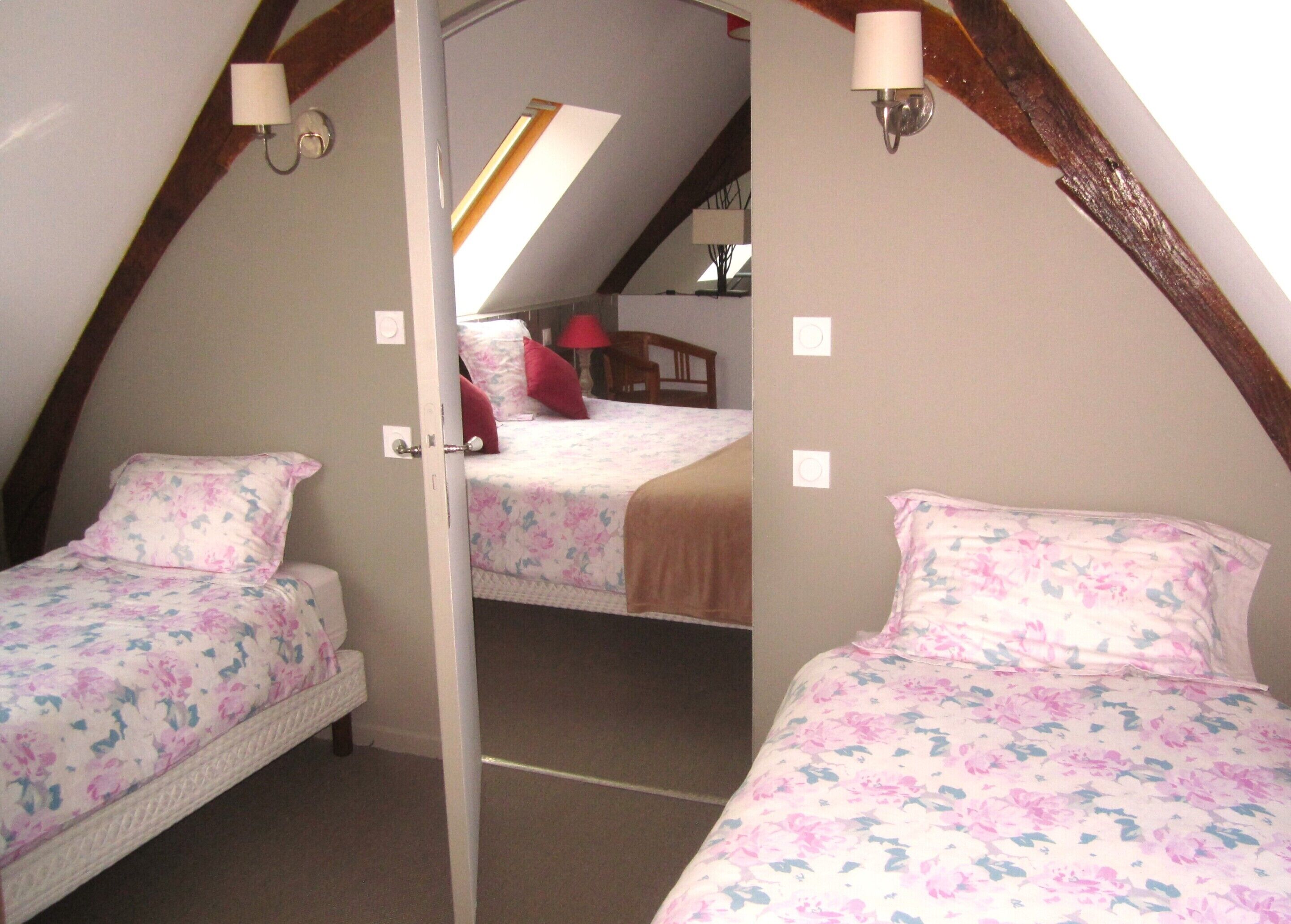 A bedroom with two beds, each with floral bedding, a skylight, and a wooden ceiling beam.