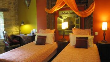 A room with two beds, each with patterned bedding and pillows, a desk with a lamp, and a chair.