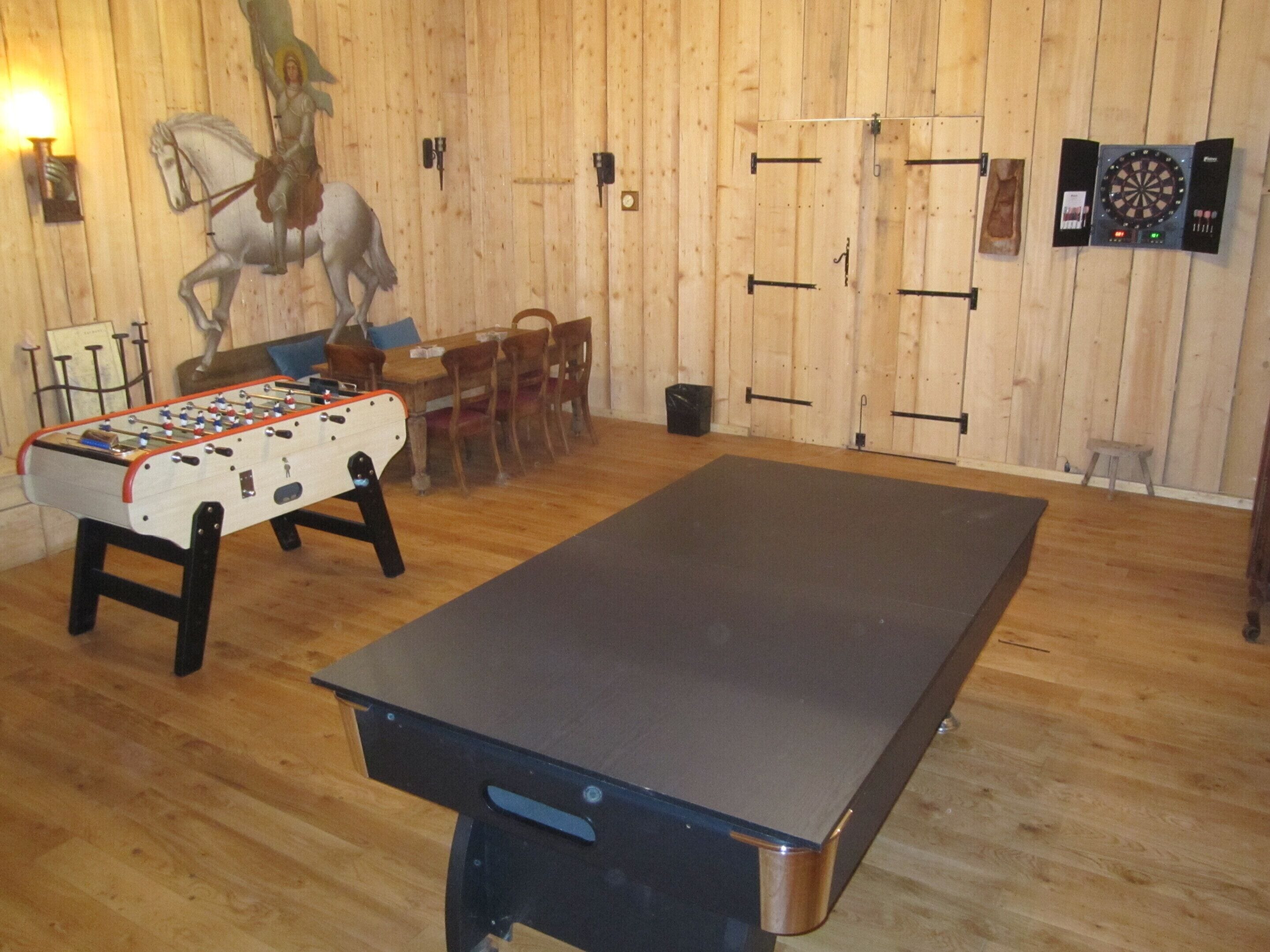 A room with a foosball table, a dartboard, and a billiards table.