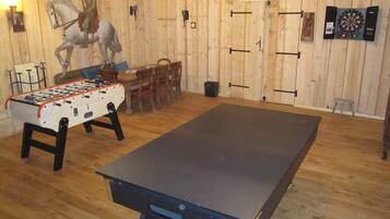 A room with a foosball table, a dartboard, and a billiards table.