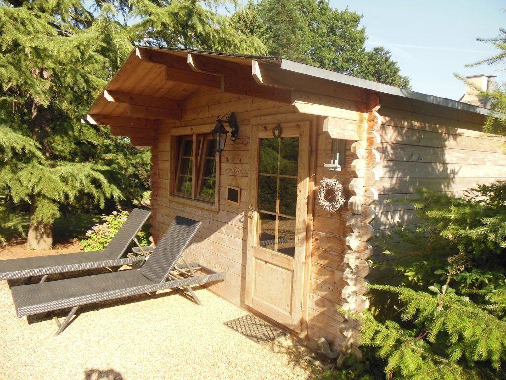 Een houten chalet met een veranda, twee lounge stoelen en een deur versierd met een krans.