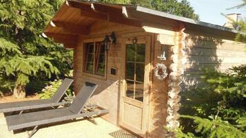 Een houten chalet met een veranda, twee lounge stoelen en een deur versierd met een krans.