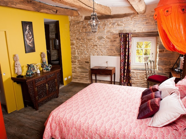 Un dormitorio con pared de piedra, cama de madera, cómoda y ventana con cortinas.
