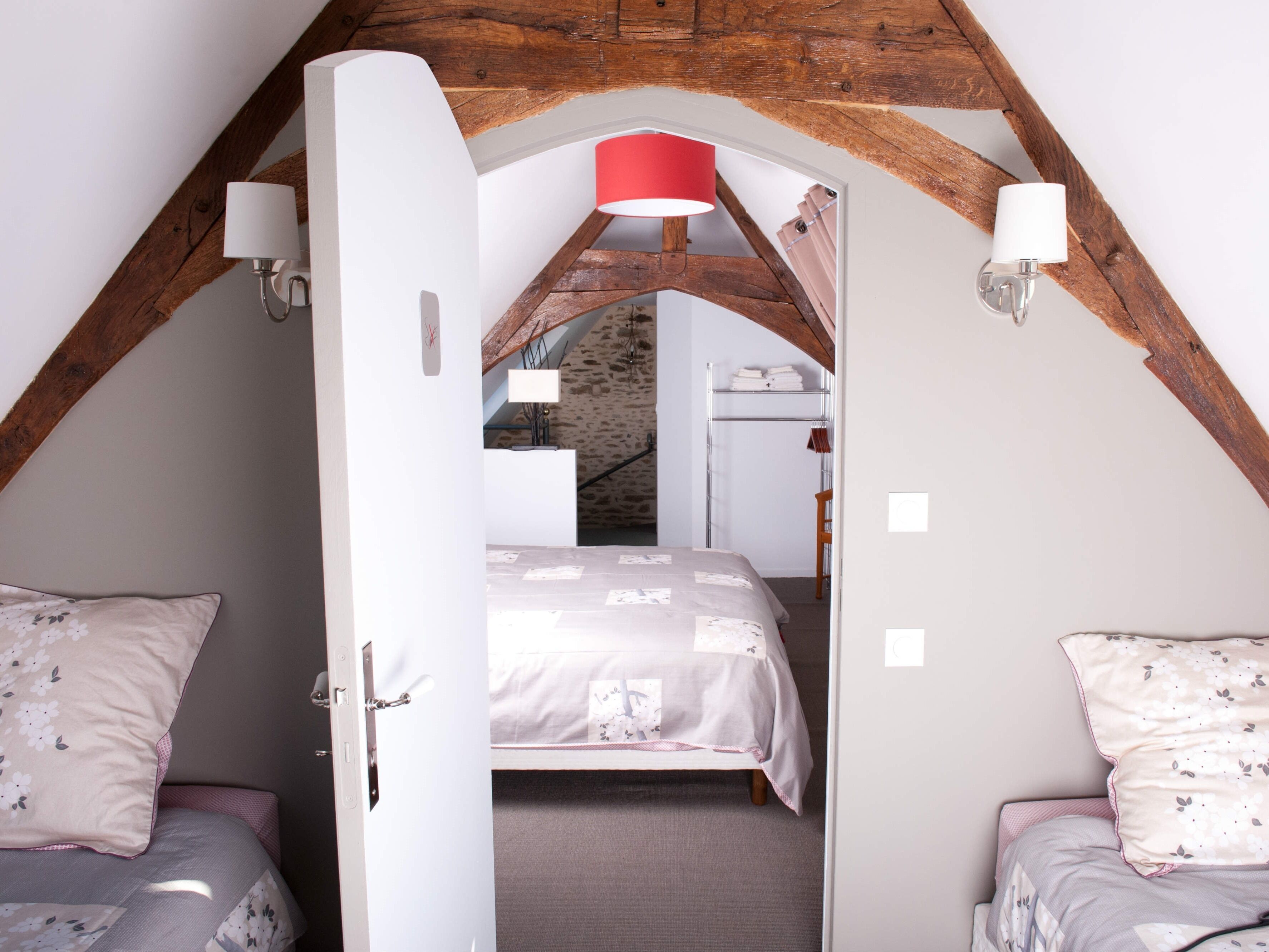 A bedroom with a sloped ceiling, a bed with a floral bedspread, two bedside tables with lamps, and a wooden staircase leading to an upper level.
