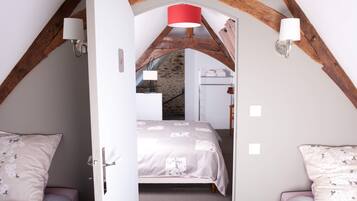 A bedroom with a sloped ceiling, a bed with a floral bedspread, two bedside tables with lamps, and a wooden staircase leading to an upper level.