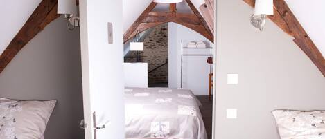 A bedroom with a sloped ceiling, a bed with a floral bedspread, two bedside tables with lamps, and a wooden staircase leading to an upper level.