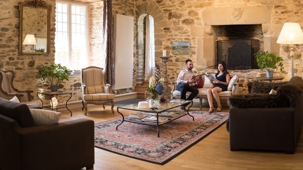 A stone-walled living room with a fireplace, a large window, and a cozy seating area. - Manoir Desnachez (Taupont)