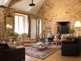 Un salon aux murs de pierre, doté d’une cheminée, d’une grande fenêtre et d’un coin salon confortable.