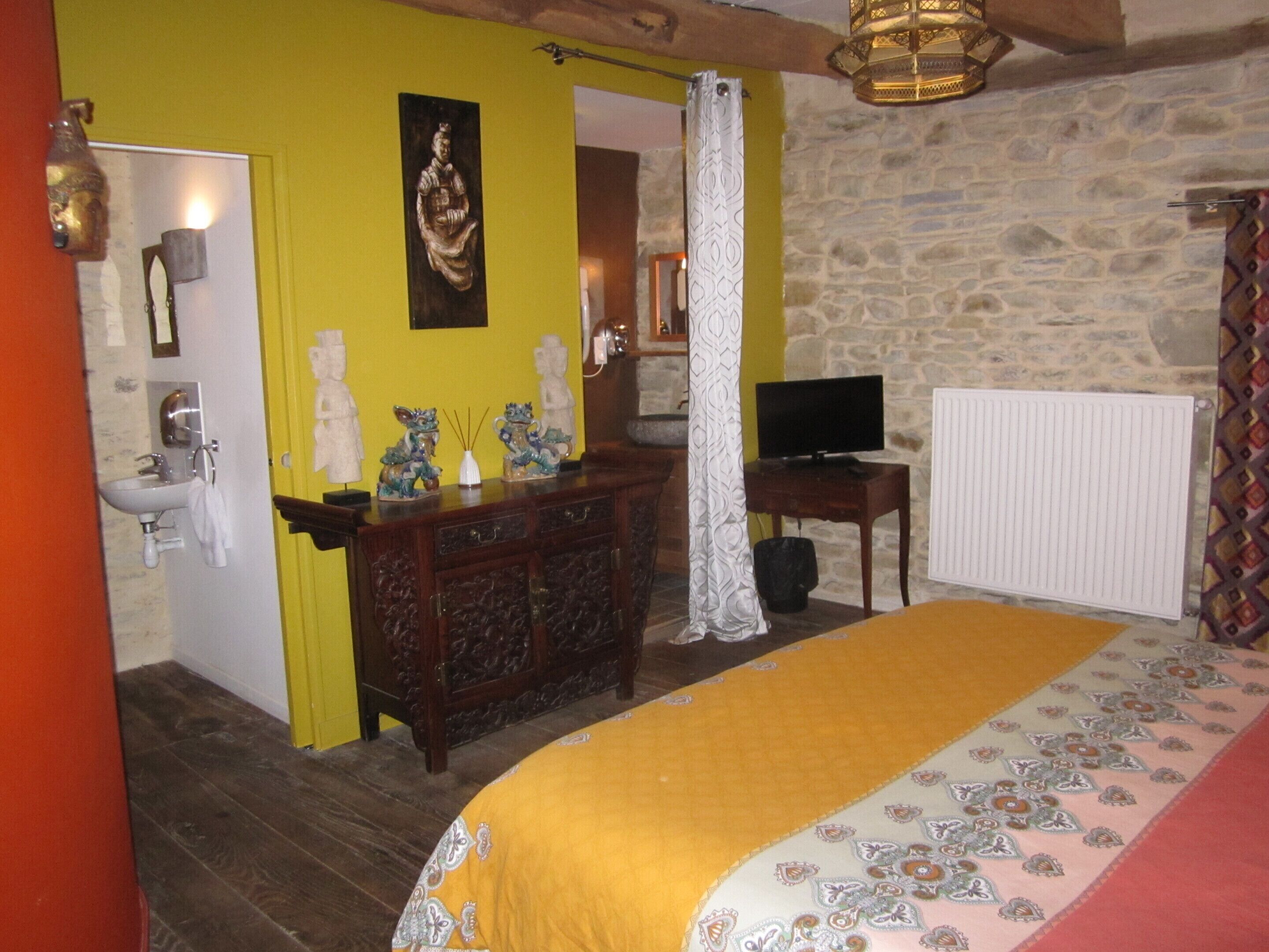 Un dormitorio con cama, cómoda, televisor y pared de piedra.