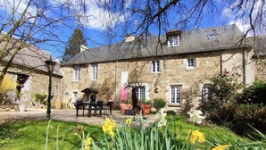 A stone building with a garden in front, including a table and chairs, and a statue of a deer. - Manoir Desnachez (Taupont)