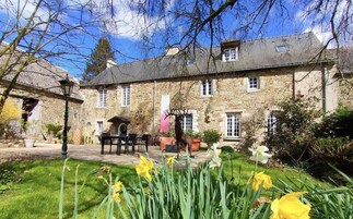 Un bâtiment en pierre avec un jardin devant, comprenant une table et des chaises, ainsi qu’une statue de cerf.