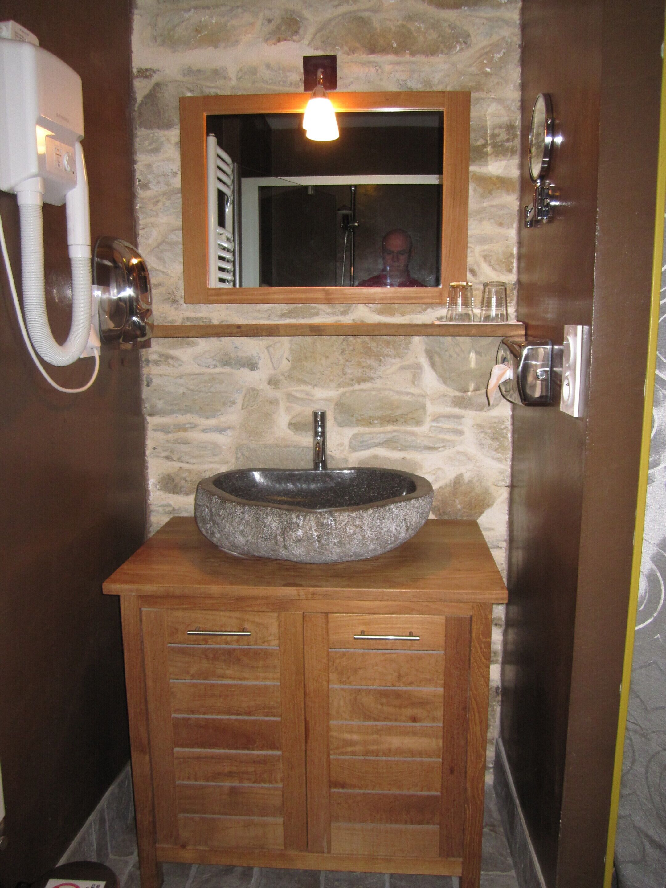 A bathroom with a stone sink, wooden vanity, a mirror, and a hairdryer.