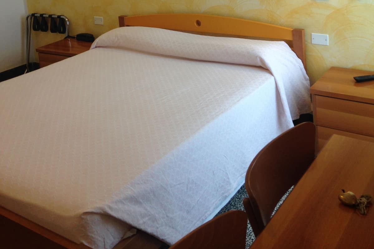 A hotel room with a bed, a wooden headboard, two bedside tables, a nightstand, a chair, a desk, and a wall-mounted picture.