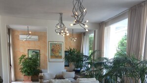 Un vaste espace de vie aménagé avec des meubles en osier, une table basse en verre et de grandes fenêtres dotées de rideaux.