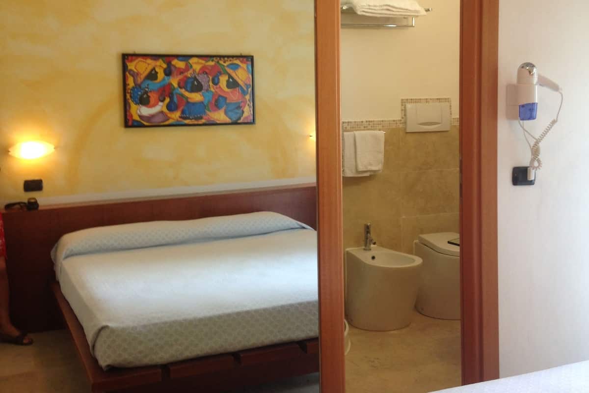 A hotel room with two beds, a bathroom with a sink and toilet, and a colorful painting on the wall.
