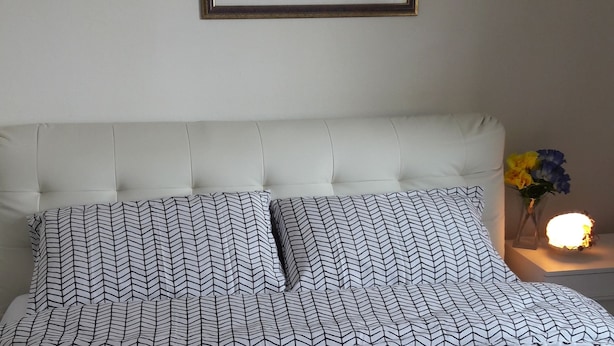Un lit bien fait, recouvert d’une courtepointe à motifs à pois et chevrons, un oreiller blanc à motifs chevrons et un tableau encadré accroché au mur.