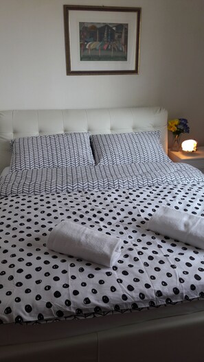 Un lit bien fait, recouvert d’une courtepointe à motifs à pois et chevrons, un oreiller blanc à motifs chevrons et un tableau encadré accroché au mur.