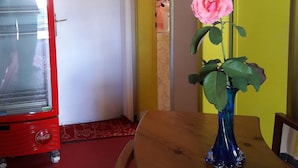 Un coin repas avec une table en bois, un vase contenant une fleur rose, un réfrigérateur rouge et une porte jaune.
