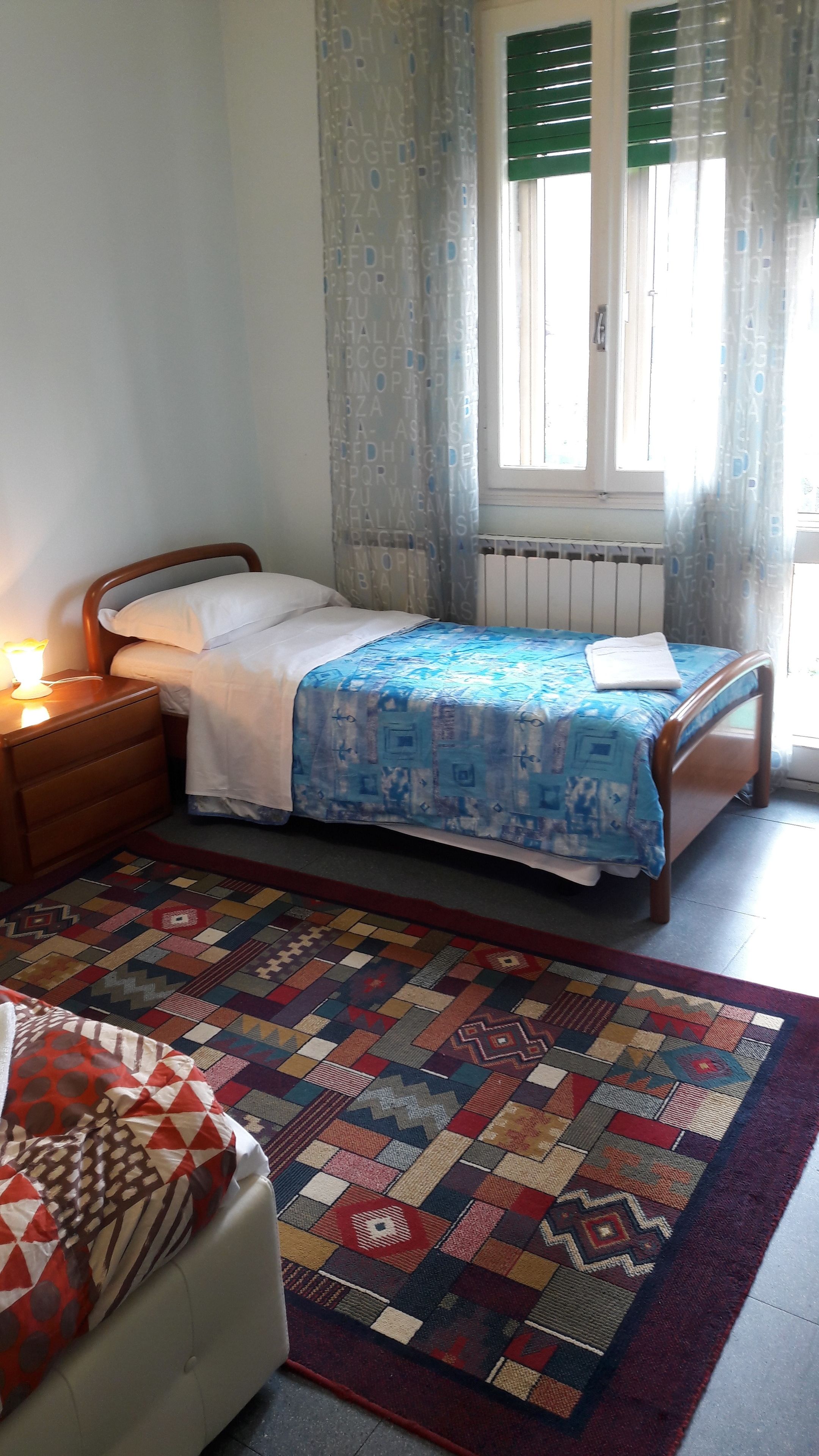 A bedroom with a bed, a nightstand, a window with curtains, and a patterned rug.
